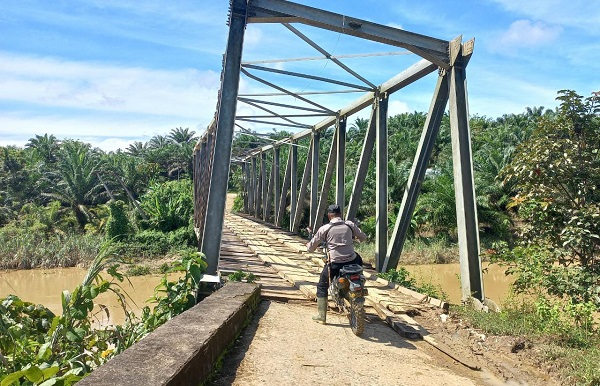 Polisi melakukan patroli melintasi jembatan penghubung Peunaron Baru – Ranto Panjang Bedari dan Sri Mulya, Kec. Peunaron, Aceh Timur, terlihat miring dan terancam roboh ke sungai. Foto diambil baru-baru ini. Waspada